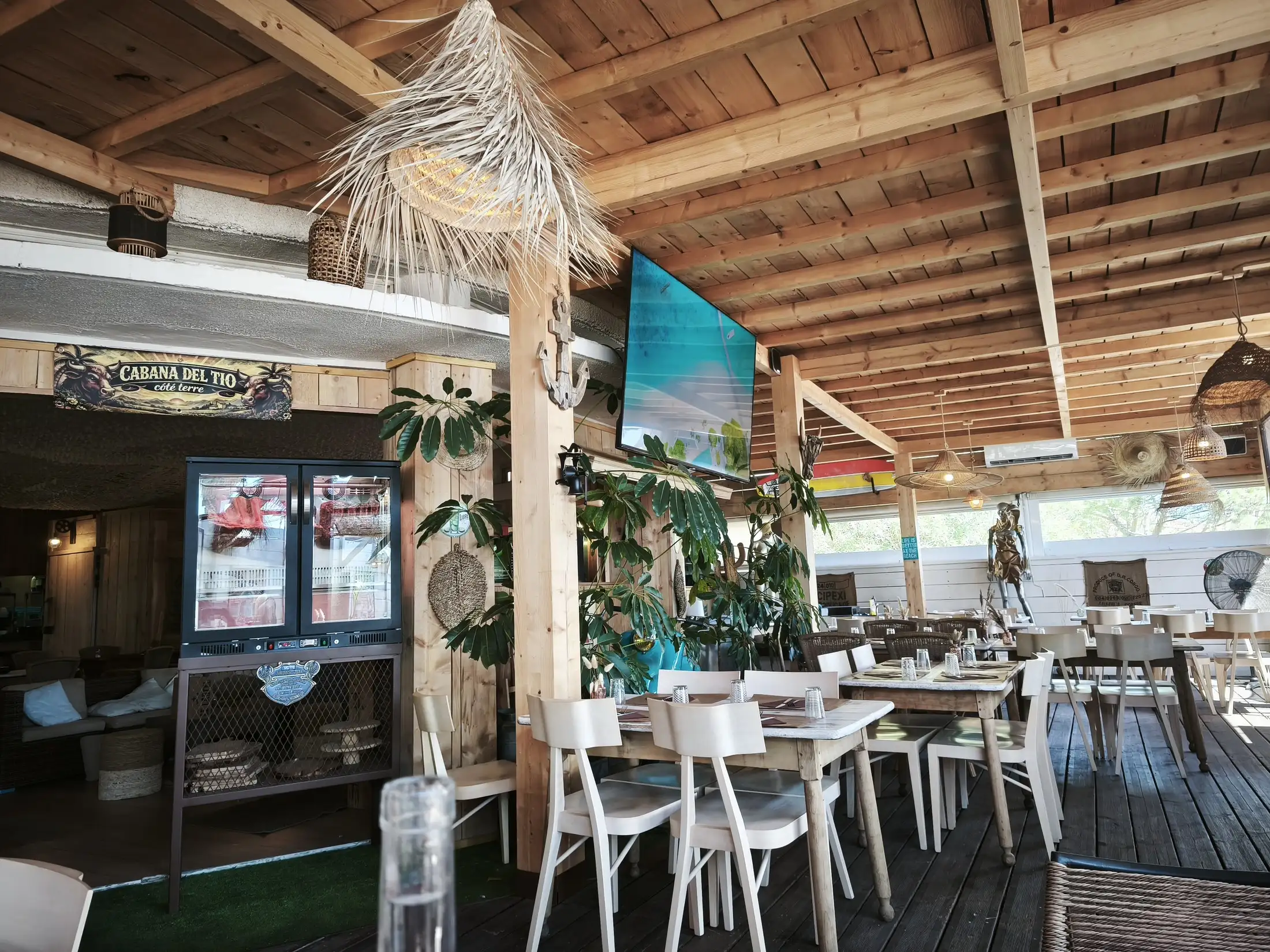 La salle couverte du restaurant : tables et chaises en bois clair sous la charpente
