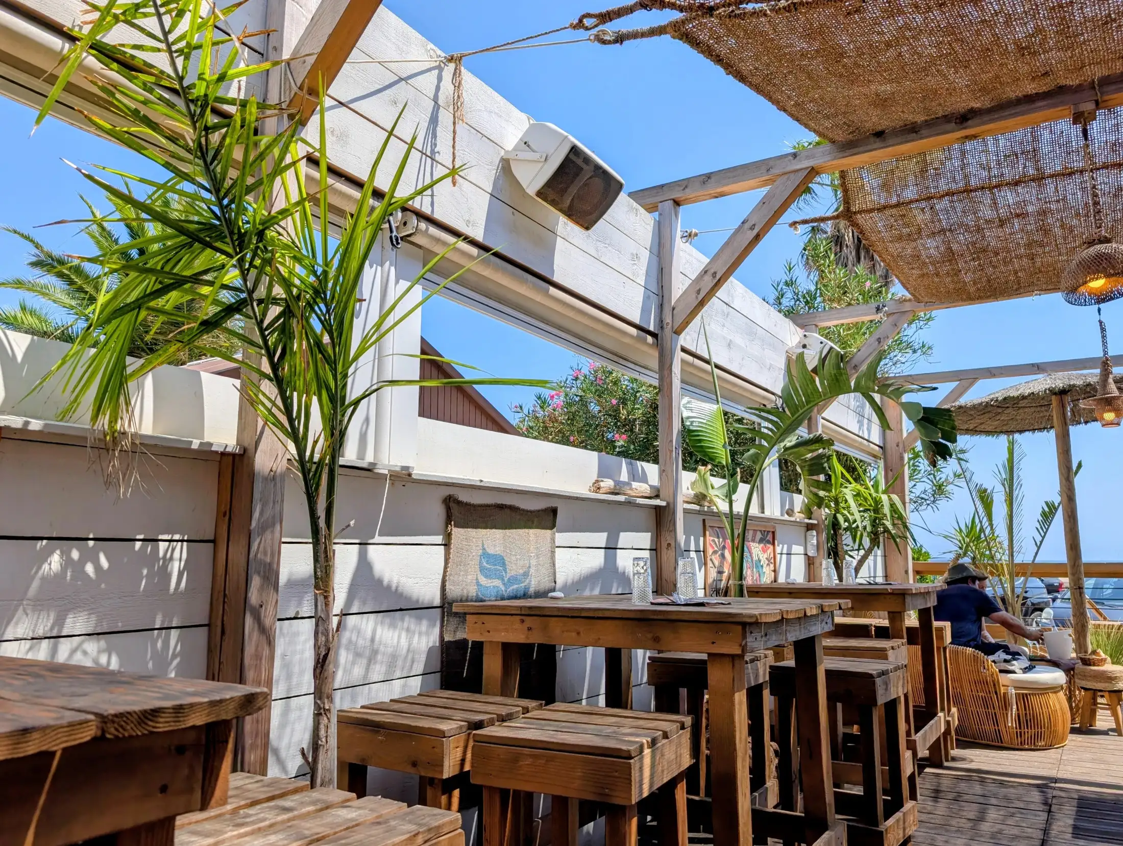 La terrasse couverte du Cabana del Tio : tables hautes et tabourets en bois brut sous une voile d'ombrage